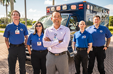 Five team members posing in front of an ambulance