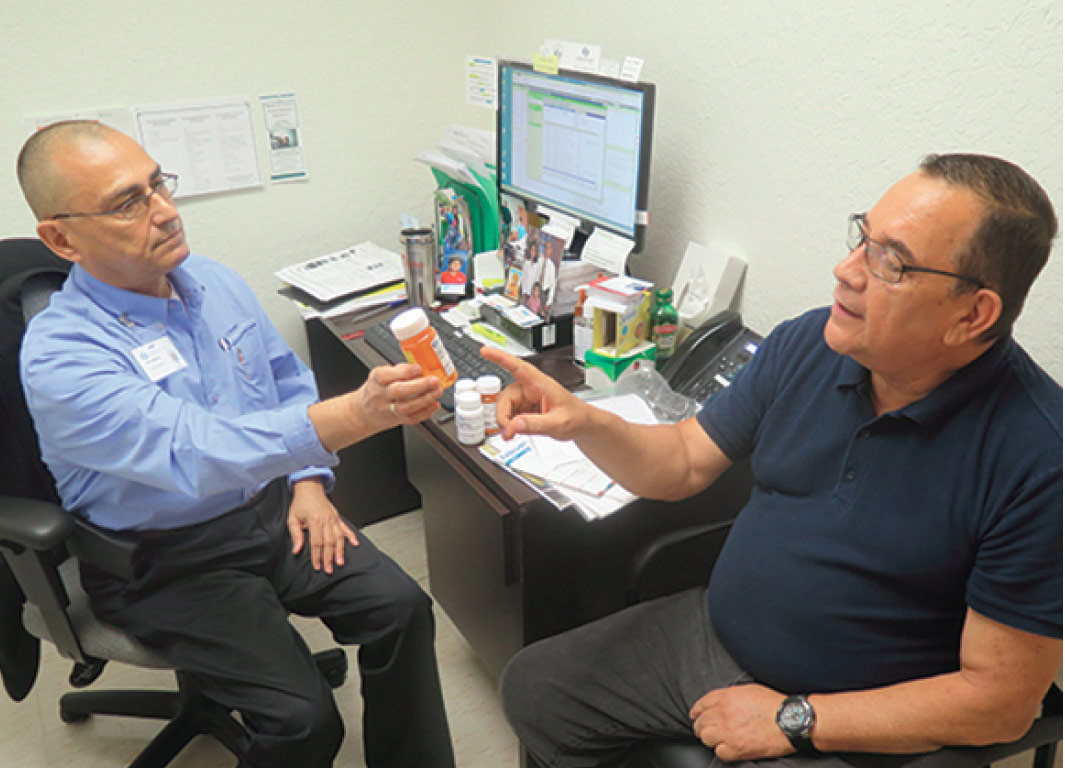 Marco holding a bottle of pills explains a medication to a patient