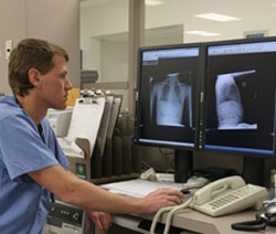 A doctor reviews two x rays on two computer monitors