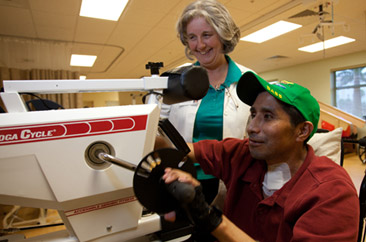 Pablo using his arms to peddle a Saratoga Cycle while Dotty assists him