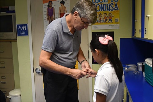 Antonio Artero, RN checking the hand of an elementary school girl
