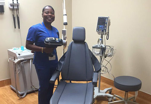 Tanya standing next to a dentist chair while holding dental equipment