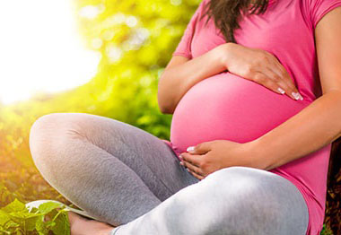 A pregnant woman sits outside on the ground in the sun caressing her stomach