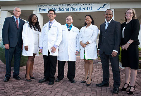 Group stands out front of the Lakeside entrance under a banner congratulating the residents