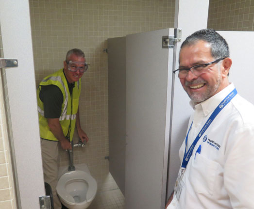 Rick standing in a toilet stall to the side of the toilet performing maintenance.