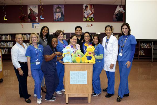 One Brumback Dental employee in the group brushes the teeth of the blue stuffed animal on the podium