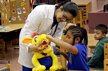 A girl plays with a yellow stuffed animal held by a member of the Brumback Dental staff.