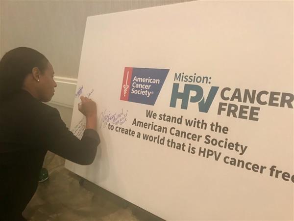 Noelle Stewart signing a large HPV cancer free banner.