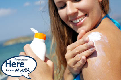 A woman in a bathing suite applies sun screen to her shoulder