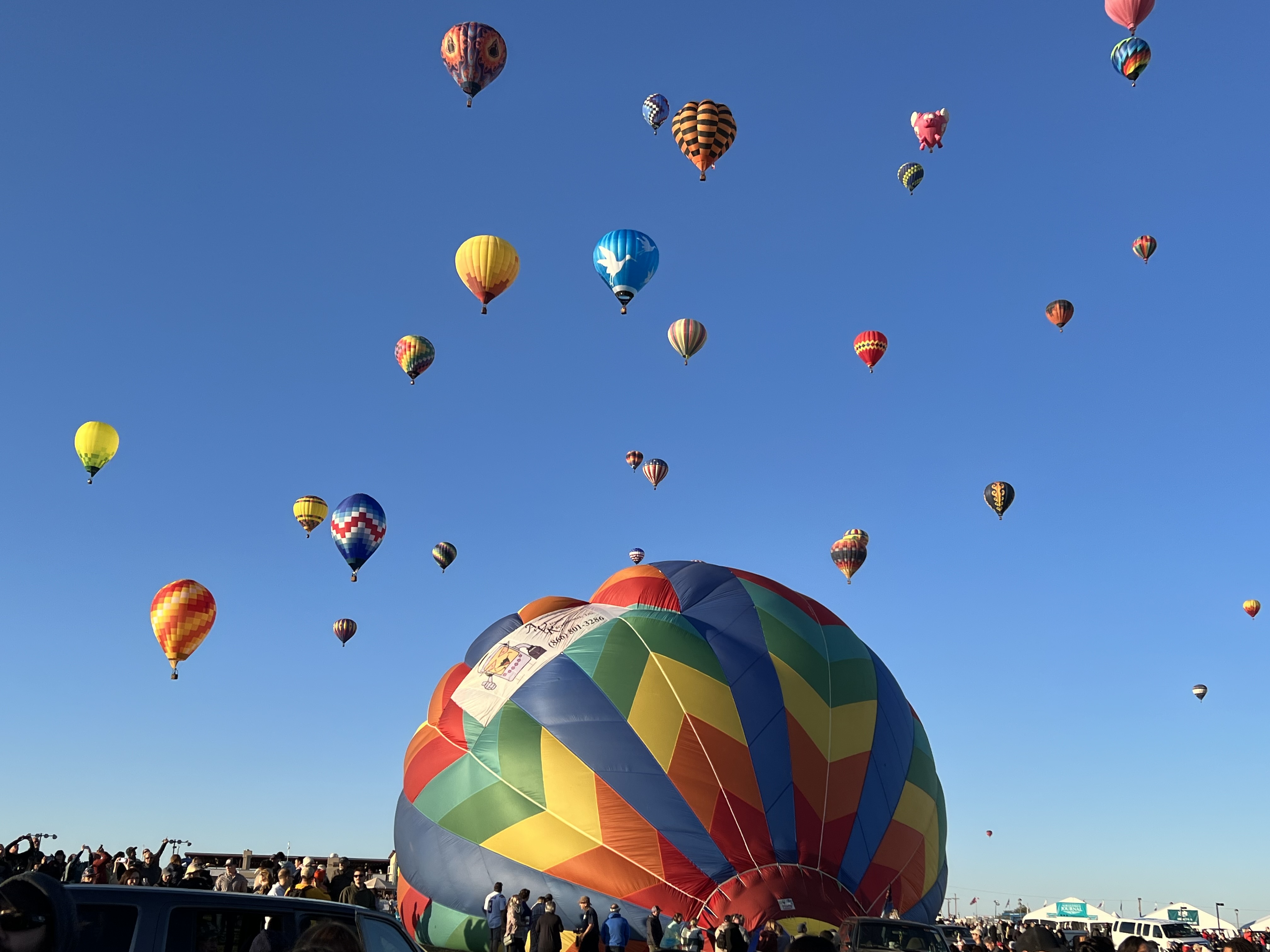 A balloon fills in the foreground prepares for liftoff while other balloons pepper the sky