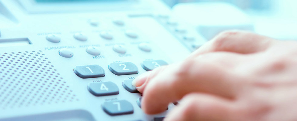 Closeup photo of a hand dialing a desk phone